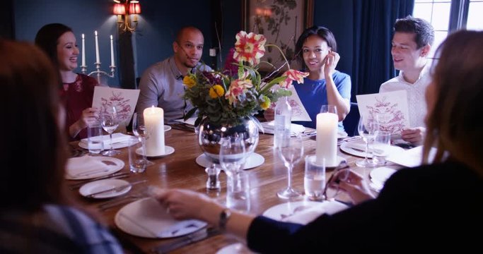 4K Happy friends group of mixed ages chatting as they look at menus in classy restaurant