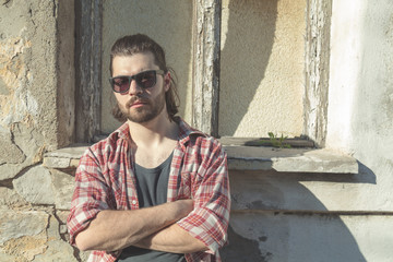 Obraz premium Man with beard and long hair posing in front of a ruined house.