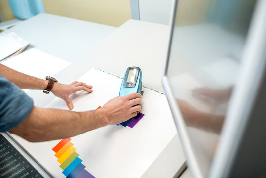 Measuring color on the paper print with spectrometer tool at the operating desk of the printing plant