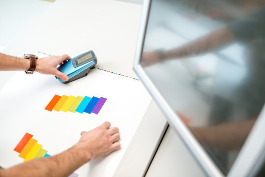 Measuring color on the paper print with spectrometer tool at the operating desk of the printing plant