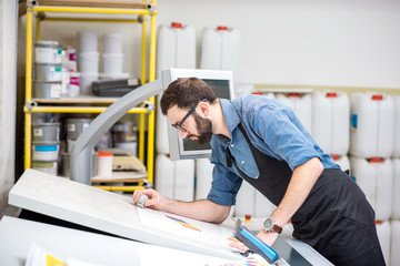 Worker checking the quality of the printing with magnifying glass on the operating table of the...