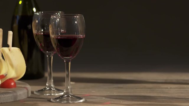 Cheese and wine tasting. Different types of cheese wedges, cheese skewered appetizers, and glasses with red wine on wooden table. Dolly shot