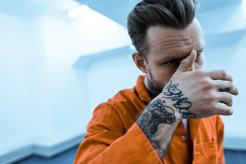 tattooed prisoner covering face with hand