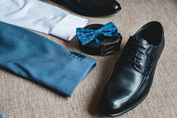 Suit, blue bow tie, leather black shoes and belt. Grooms wedding morning. Close up of modern man accessories