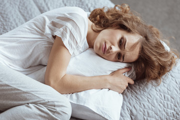 Stressful life. Top view on a poor woman looking sad while lying on her bed and struggling with depressing thoughts.