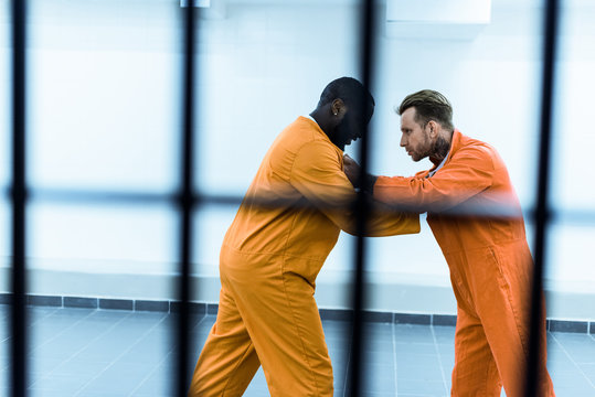 side view of multiethnic prisoners fighting behind prison bars