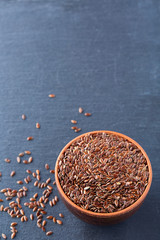 Close-up picture of flax seeds in a clay bowl isolated on dark background.