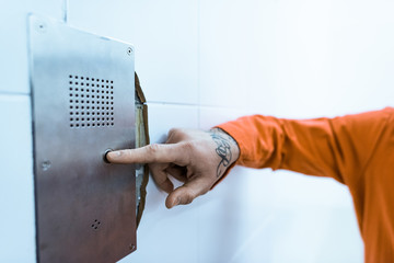 cropped image of tattooed prisoner in orange uniform pressing button in prison cell