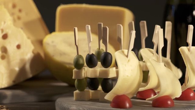 Cheese and wine tasting. Different types of cheese wedges, cheese skewered appetizers, and glasses with red wine on wooden table. Dolly shot