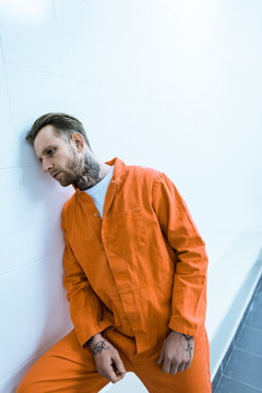tattooed prisoner leaning on wall in prison cell