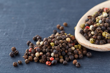 Top view on composition of peppercorns in wooden spoon on dark background, close-up.