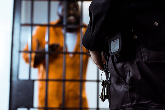 cropped image of security guard standing near prison bars with keys