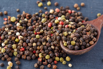 Top view on composition of peppercorns in wooden spoon on dark background, close-up.