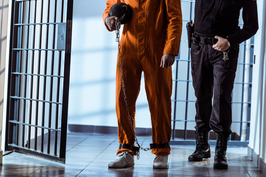 cropped image of prison officer leading prisoner carrying weight tethered to leg