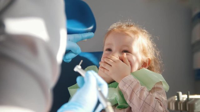 Little cute girl in the dentist's office does not want to be treated, resisting and closing her mouth with her hands