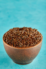 Close-up picture of flax seeds in a clay bowl isolated on blue background.