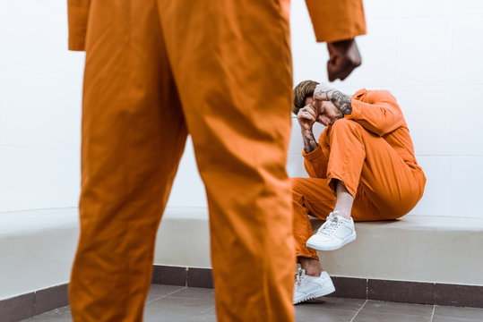 cropped image of african american prisoner standing with fist, other prisoner covering face