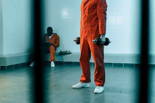 cropped image of prisoner training with dumbbells in prison room