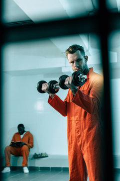 prisoner training with dumbbells in prison room behind prison bars