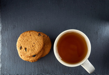 Close-up white cup of tea with chocolate cookies on dark background, top view