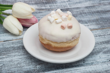 Delicious doughnut with white Cream Icing, and beautiful Tulip flowers on Wooden Rustic grey background with copy space for Text. Vertical image.