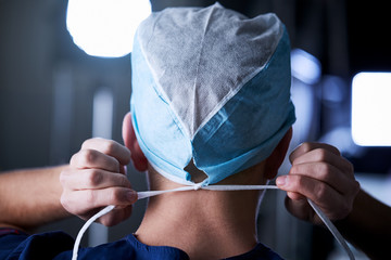 Surgeon tying surgical cap in preparation, back view