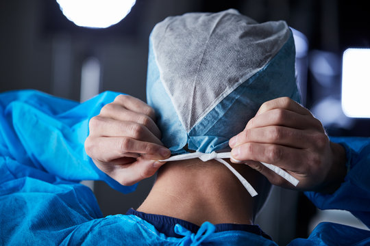 Surgeon tying surgical cap in preparation, back view