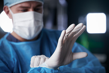 Male surgeon putting on latex gloves in preparation