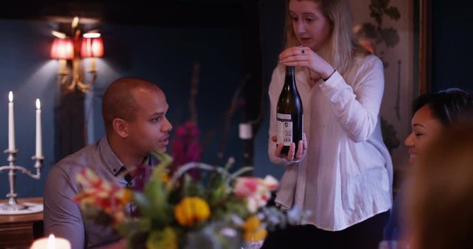 4K Cheerful waitress serves wine to adult family group in friendly restaurant