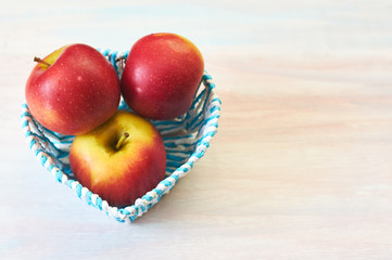 Red apples in a basket on a white wooden background