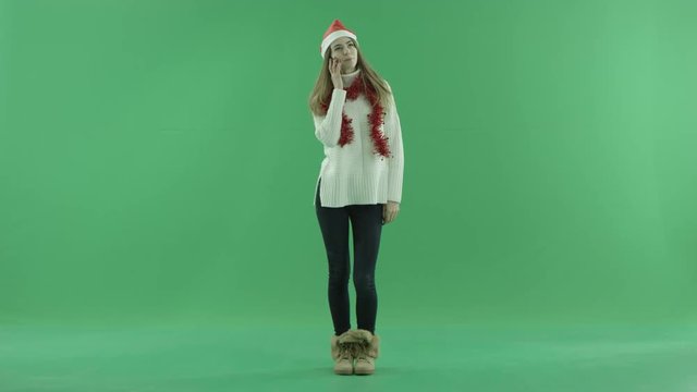 Funny young blond woman in Christmas hat talks over smartphone, chroma key on background