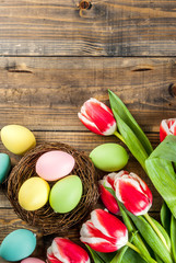 Multicolored Easter eggs with tulips flowers on wooden background,copy space top view