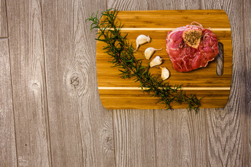 Raw veal ossobuco cross cut shank with rosemary and fresh garlic on bamboo tray