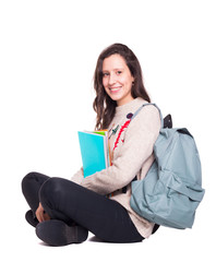 Smiling student girl sitting on the floor with legs crossed with notebooks and backpack, isolated on a white background