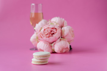Glass of wine, bouquet of peonies and white macaroons  on pink background. Space for text