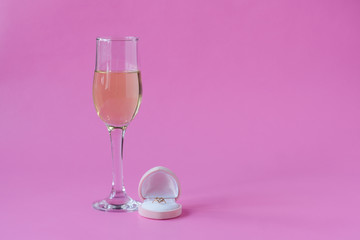 Engagement ring and glass of wine on pink background. Space for text