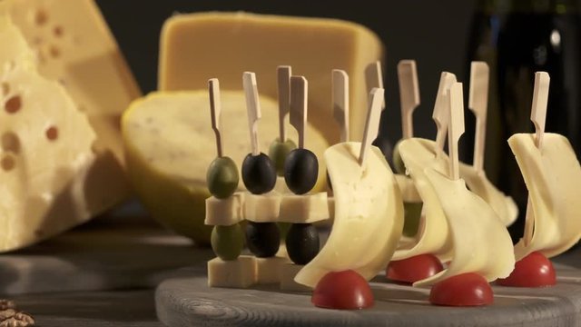 Cheese and wine tasting. Different types of cheese wedges, cheese skewered appetizers, and glasses with red wine on wooden table. Dolly shot