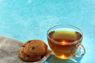 Glass cup of tea and chocolate cookies close-up on blue background.