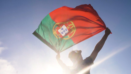Young man holding portuguese national flag to the sky with two hands at the beach at sunset portugal