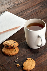 Cup of tea with cookies, workbook and a pencil on a wooden background, top view