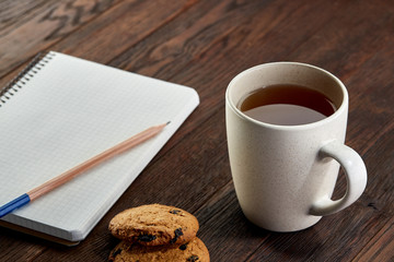 Cup of tea with cookies, workbook and a pencil on a wooden background, top view