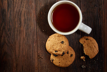 Cup of tea with cookies, workbook and a pencil on a wooden background, top view
