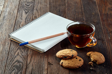 Cup of tea with cookies, workbook and a pencil on a wooden background, top view