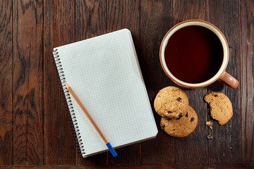 Obraz na płótnie Canvas Cup of tea with cookies, workbook and a pencil on a wooden background, top view