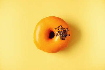 Sweet doughnut with orange glaze and chocolate on grey background. Tasty donut on pastel yellow texture, copy space, top view