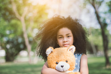 Little cute african american girl hugging embraces an amusing teddy bear against summer nature.