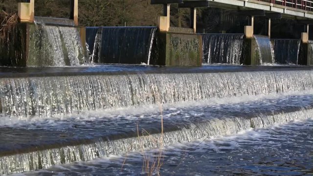 Fast flowing water cascades down the steps of a concrete weir on the river Weaver, Cheshire, Uk.