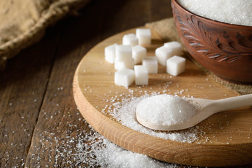 Bowl and spoon full of sugar on wooden background