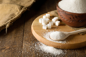 Bowl and spoon full of sugar on wooden background