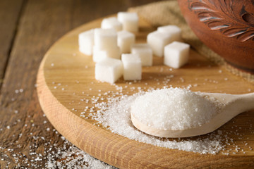 Bowl and spoon full of sugar on wooden background